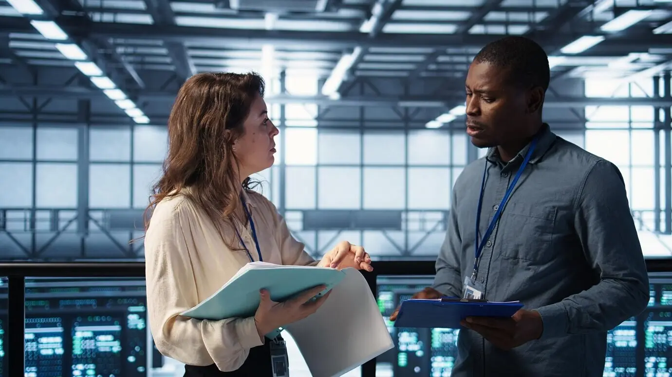 Весёлые администраторы встречаются в дата-центре для просмотра отчётов и пожимают друг другу руки.